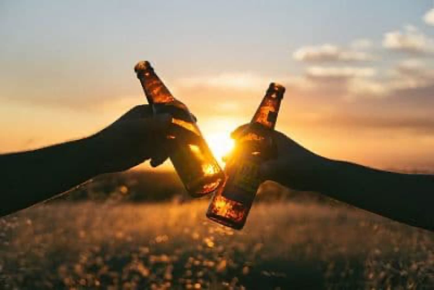 Gün batımında iki elin bira şişelerini tokuşturması