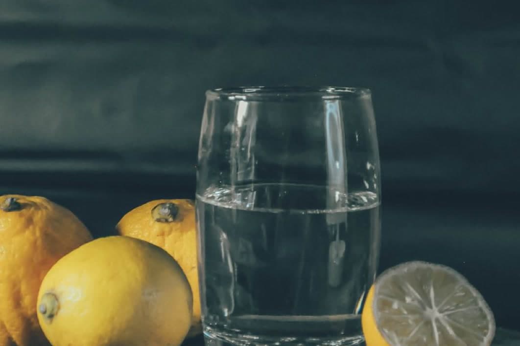 Koyu zeminde su bardağı ve yanında limonlar