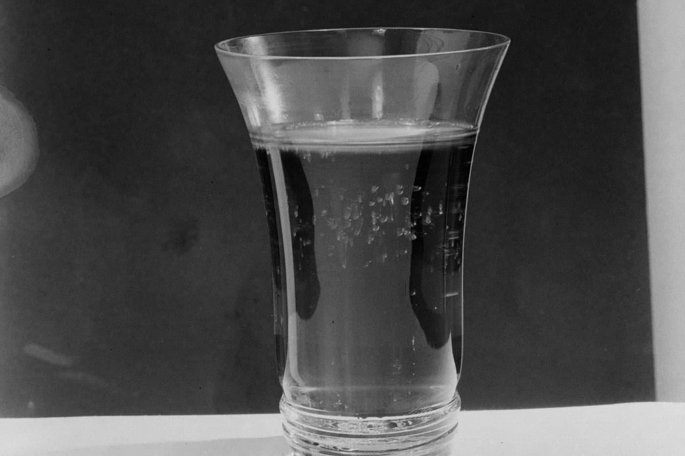 Siyah beyaz bir stüdyo fotoğrafında, koyu renkli gazlı içecek dolu bir bardak; camda kabarcıklar görünüyor