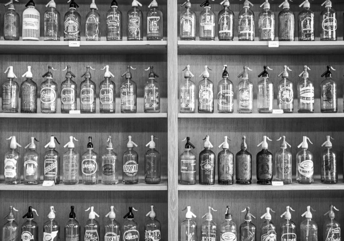 Ahşap raflarda dizili, üzerleri yazılı antika soda sifonu şişeleri