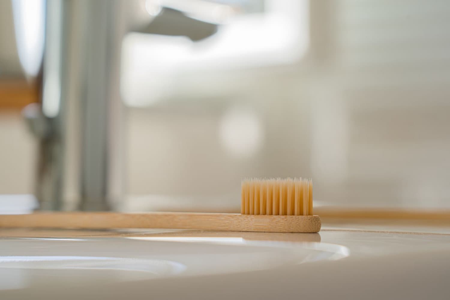 Beyaz lavabo kenarında duran ahşap saplı diş fırçası