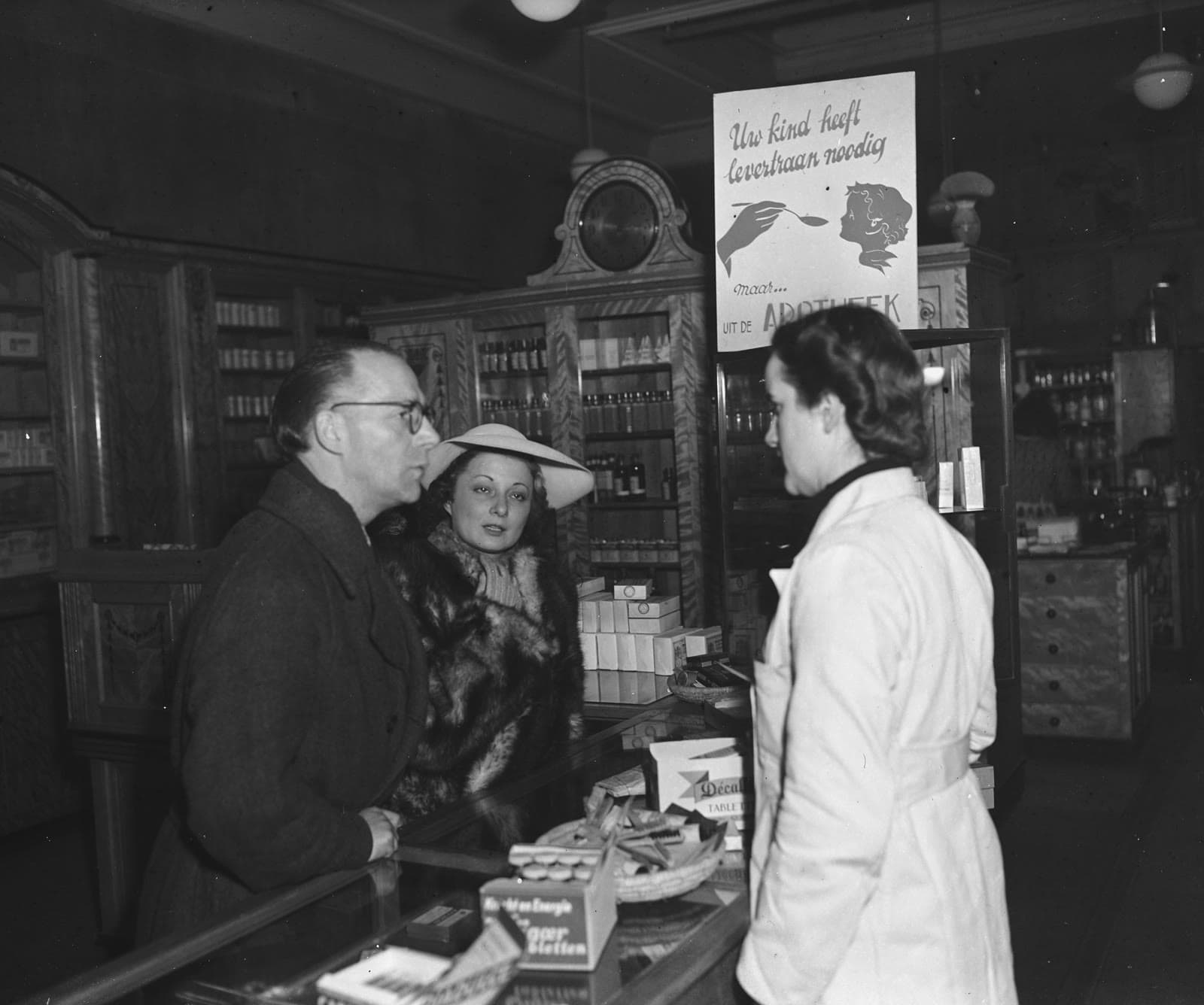 1946'da Amsterdam'da bir eczane tezgâhında müşteriler ve eczacı, arkada bir balık yağı afişi
