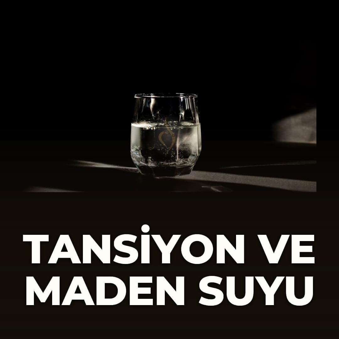 Koyu zeminde, ışık düşen bir yüzeyde duran maden suyu bardağı