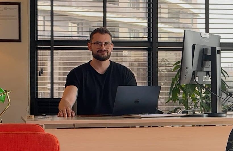 Deniz Eriş ofisinde, dizüstü bilgisayarının başında kameraya bakıyor; görüntülü görüşmede karşı tarafın gördüğü kadraj