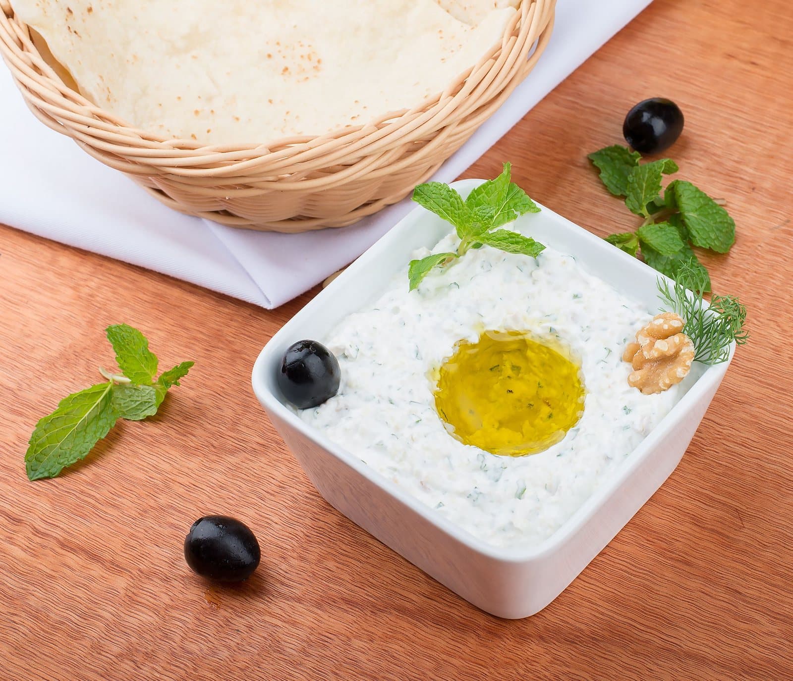 Beyaz kare kâsede yoğurtlu yeşillikli meze, ortasında zeytinyağı, yanında nane ve ekmek sepeti
