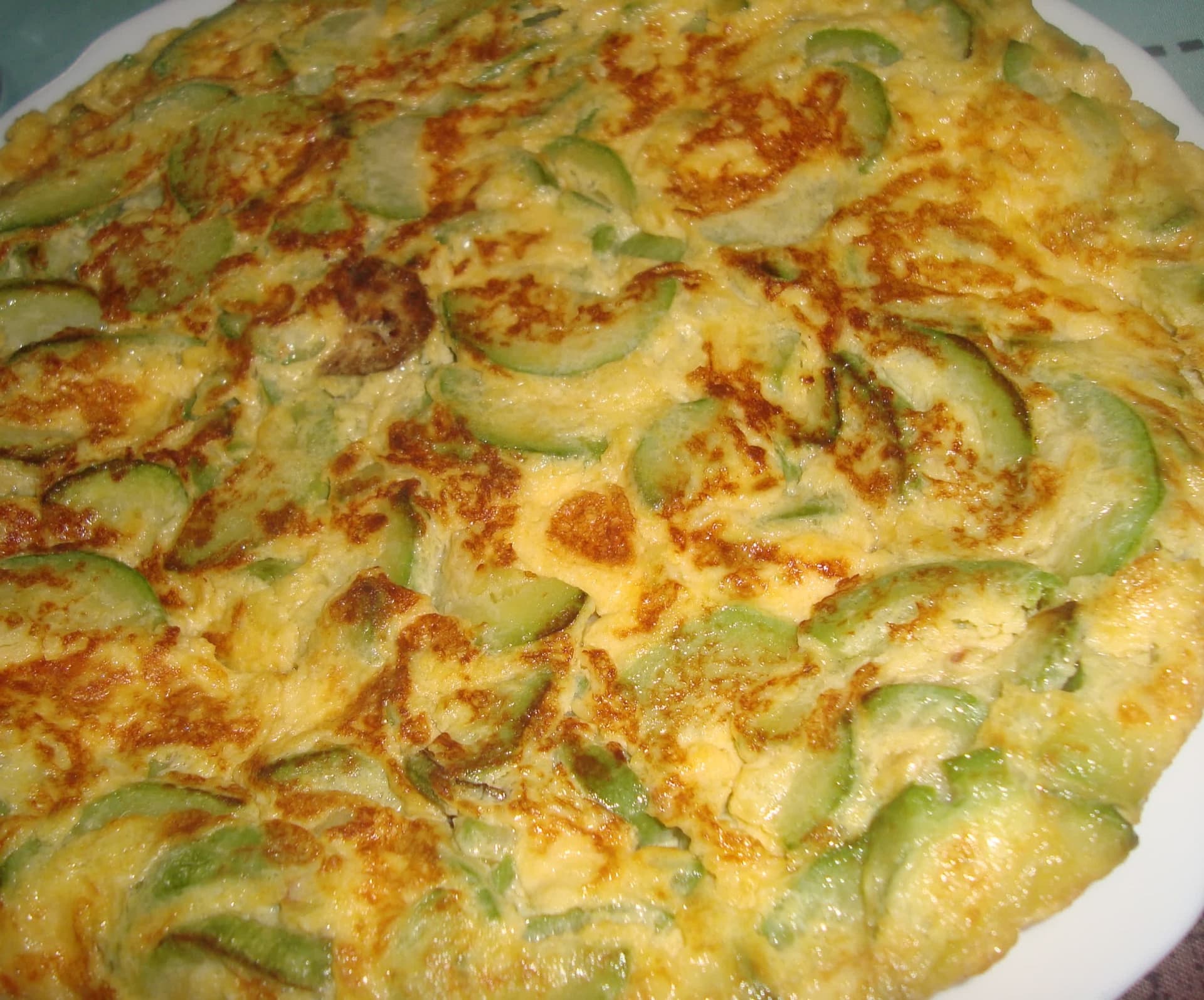 Beyaz tabakta yayılmış yuvarlak omlet, içi baştan aşağı ince kabak dilimleriyle dolu