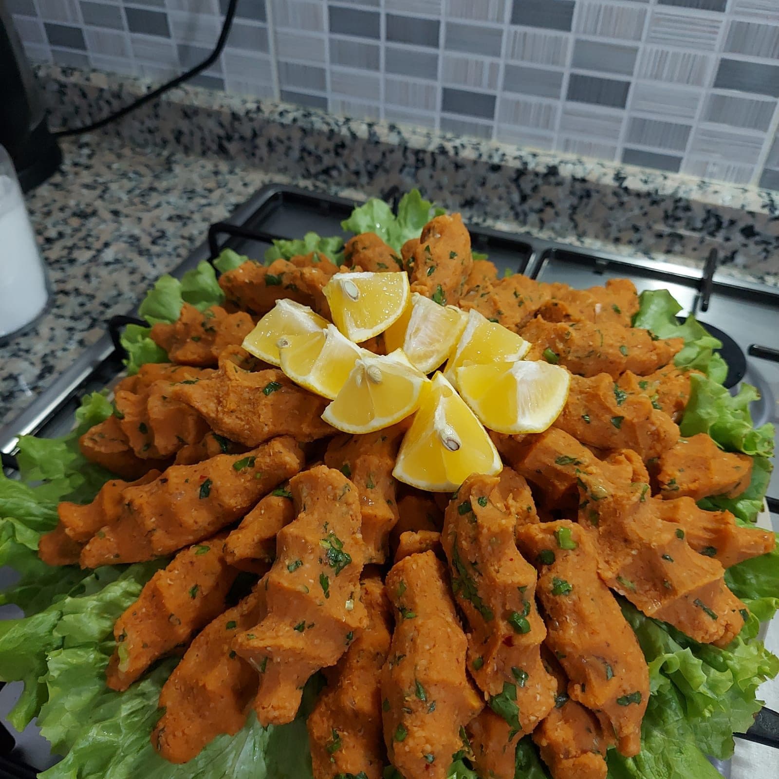 Yeşil yaprakların üzerine dizilmiş elle şekillendirilmiş mercimek köftesi, ortasında limon dilimleri