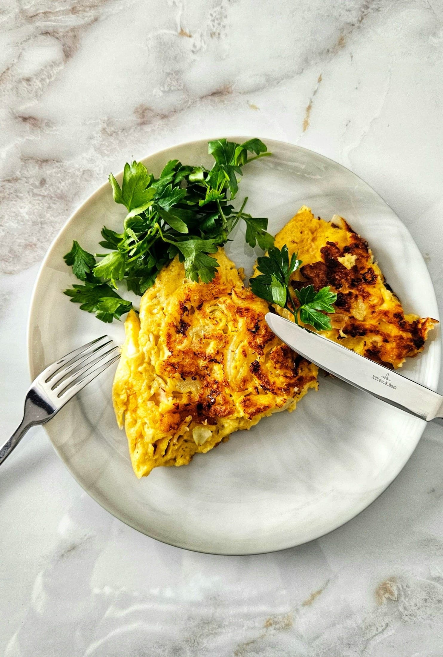 Açık mermer masada beyaz tabakta kesilmiş omlet, üzerinde maydanoz demeti