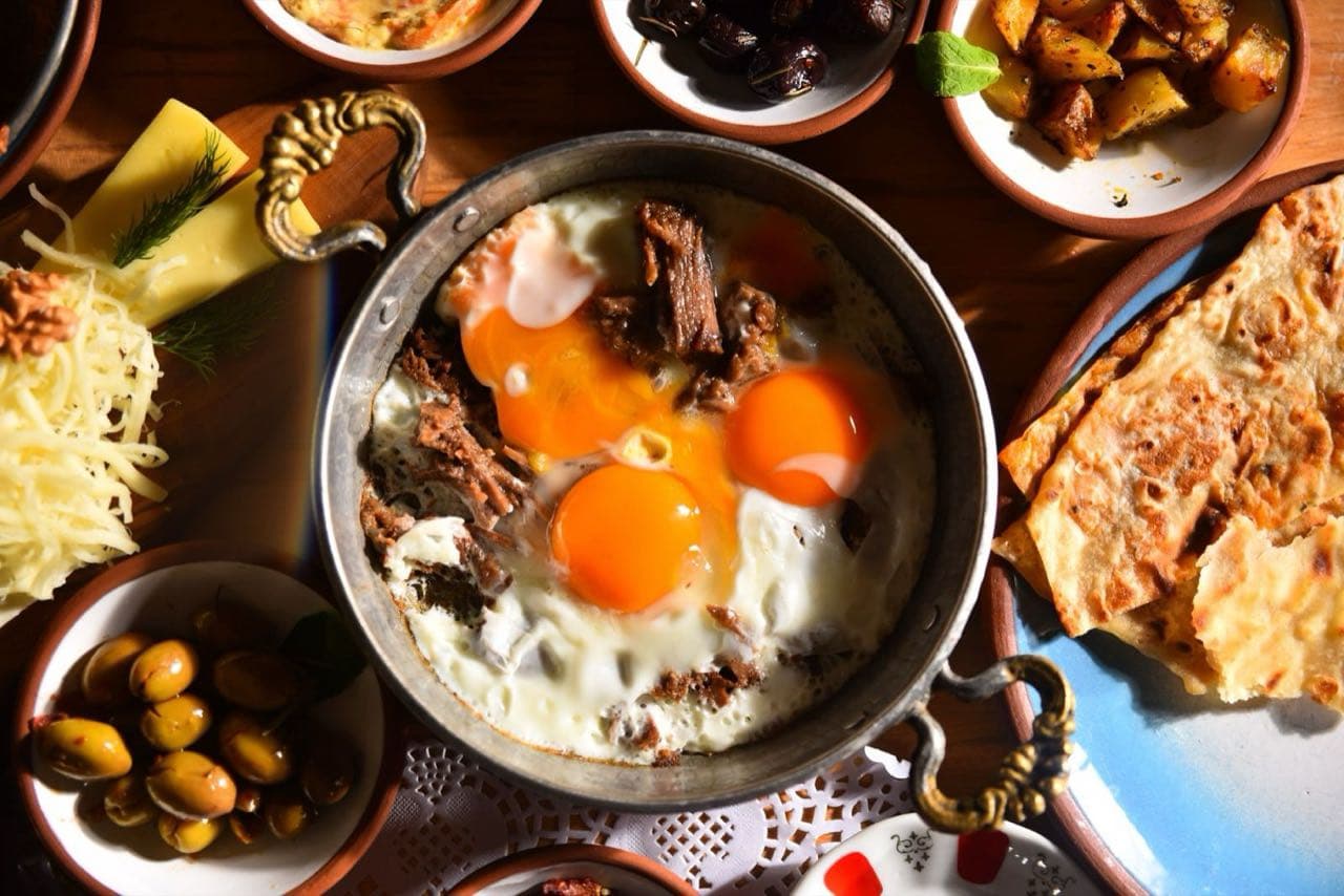 Bakır sahanda pişmiş yumurta, yanında zeytin ve kahvaltılıklar