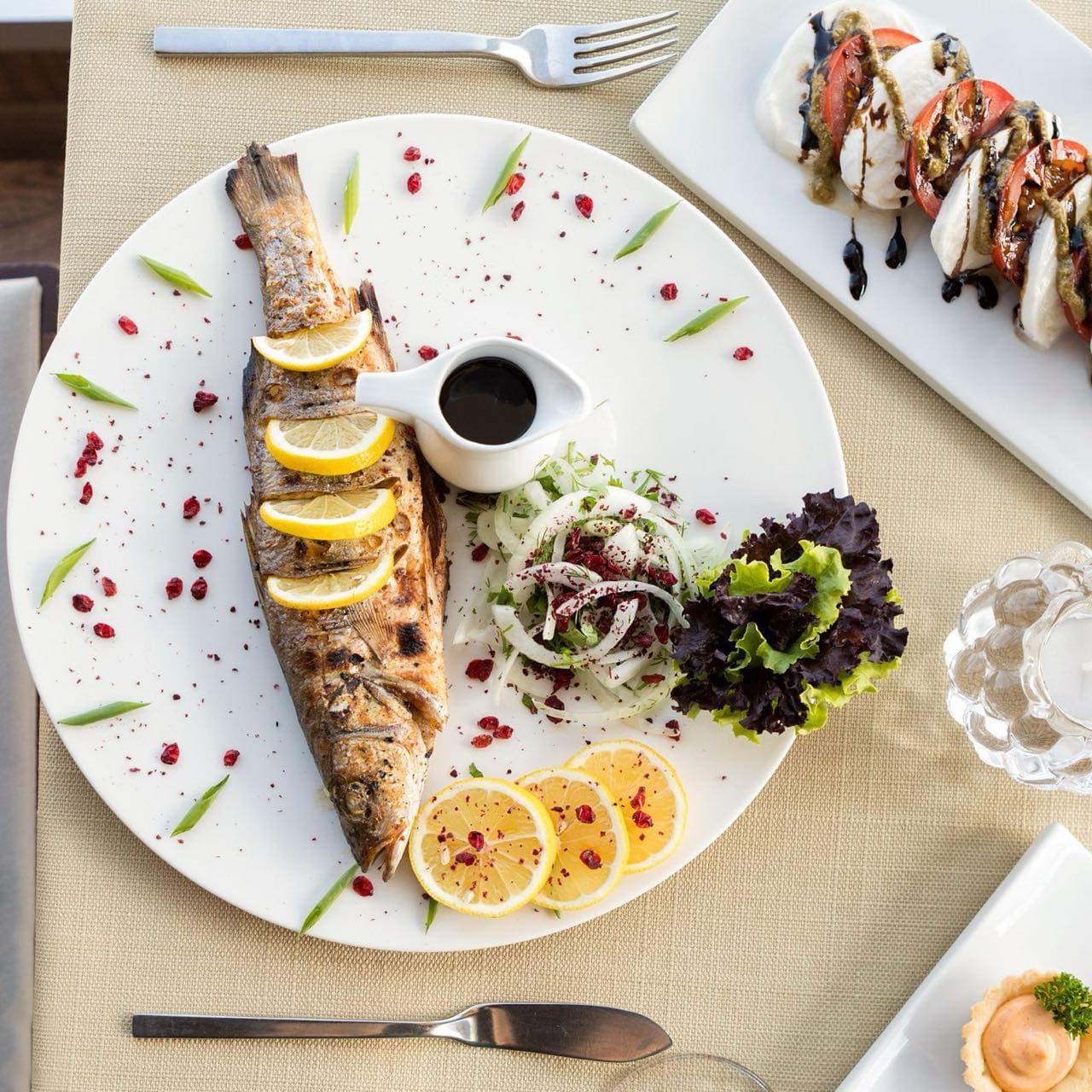 Lokanta masasında bütün ızgara balık, limon dilimleri ve yeşil salata