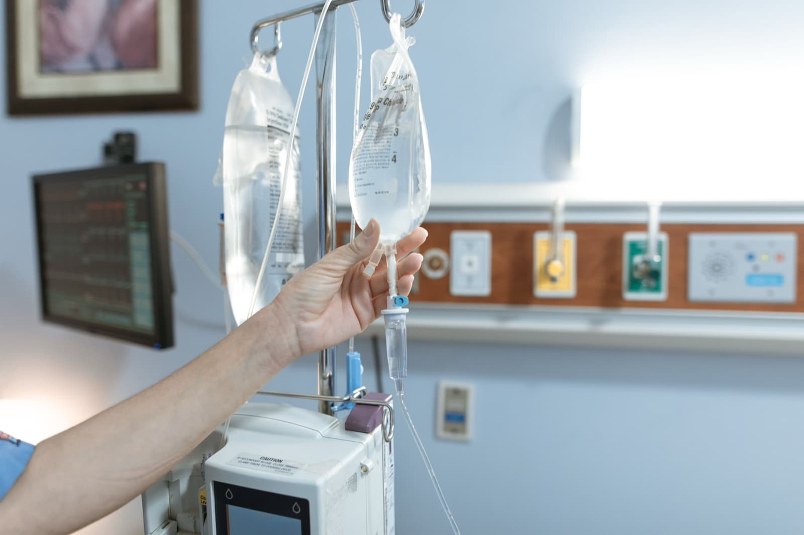 Bir sağlık çalışanının kolu serum torbasını askıya asarken, aydınlık hastane odası