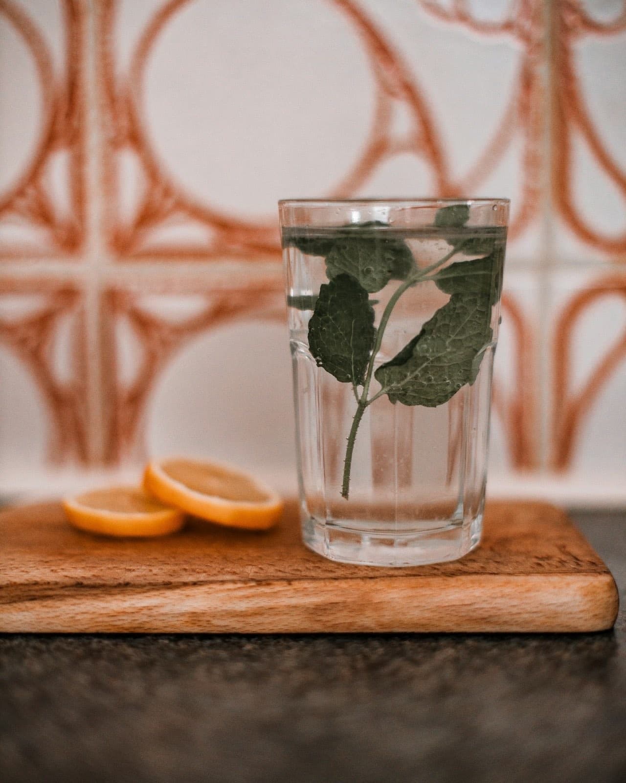 Ahşap tahtada bir bardak suda yüzen nane yaprakları, yanında limon dilimleri