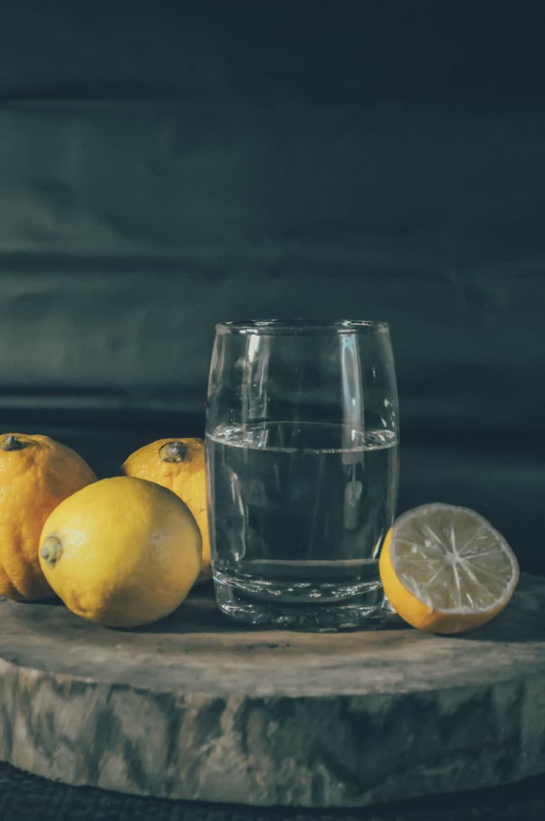Koyu zeminde su bardağı ve yanında limonlar