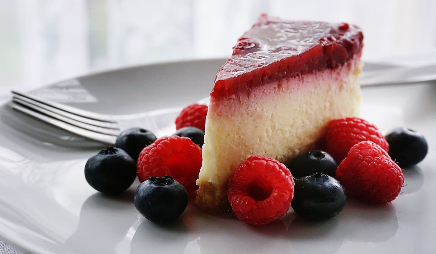Beyaz tabakta tek dilim meyveli cheesecake, üzerinde ahududu ve yaban mersini