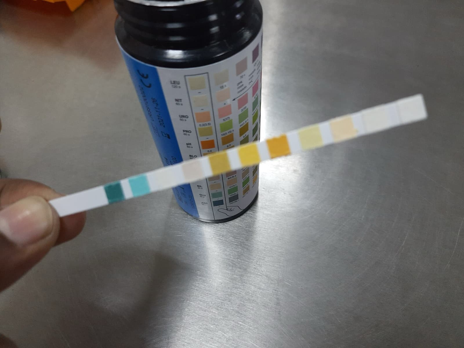 Elde tutulan idrar test stribi, kutunun üzerindeki renk skalasıyla karşılaştırılırken