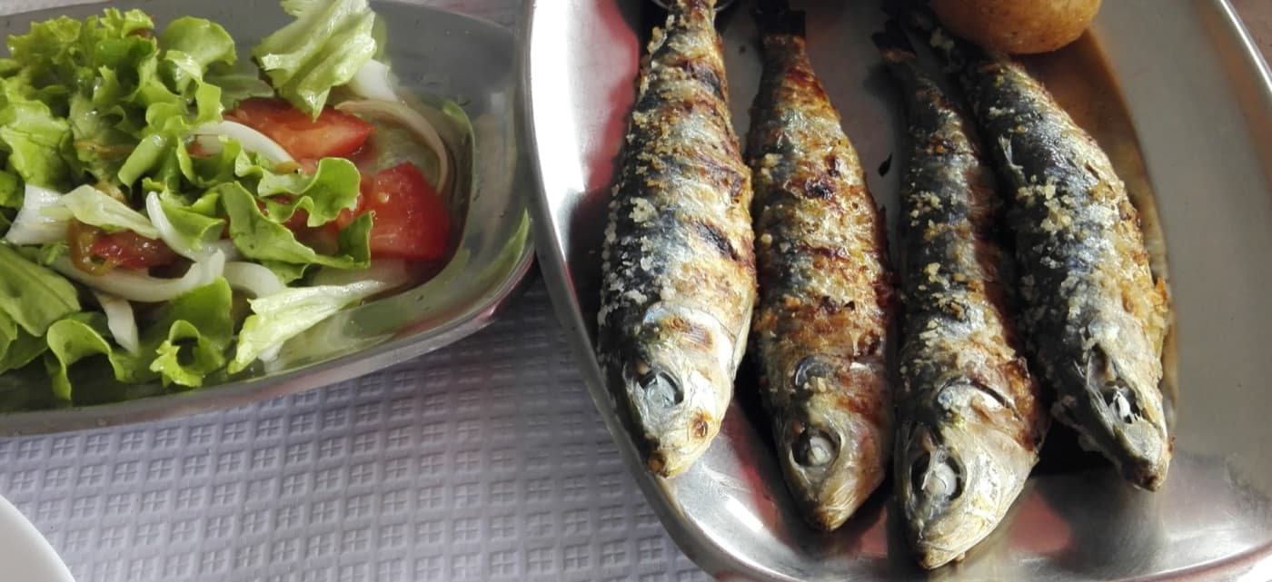 Metal tabakta ızgarada pişmiş dört sardalya, yanında yeşil salata