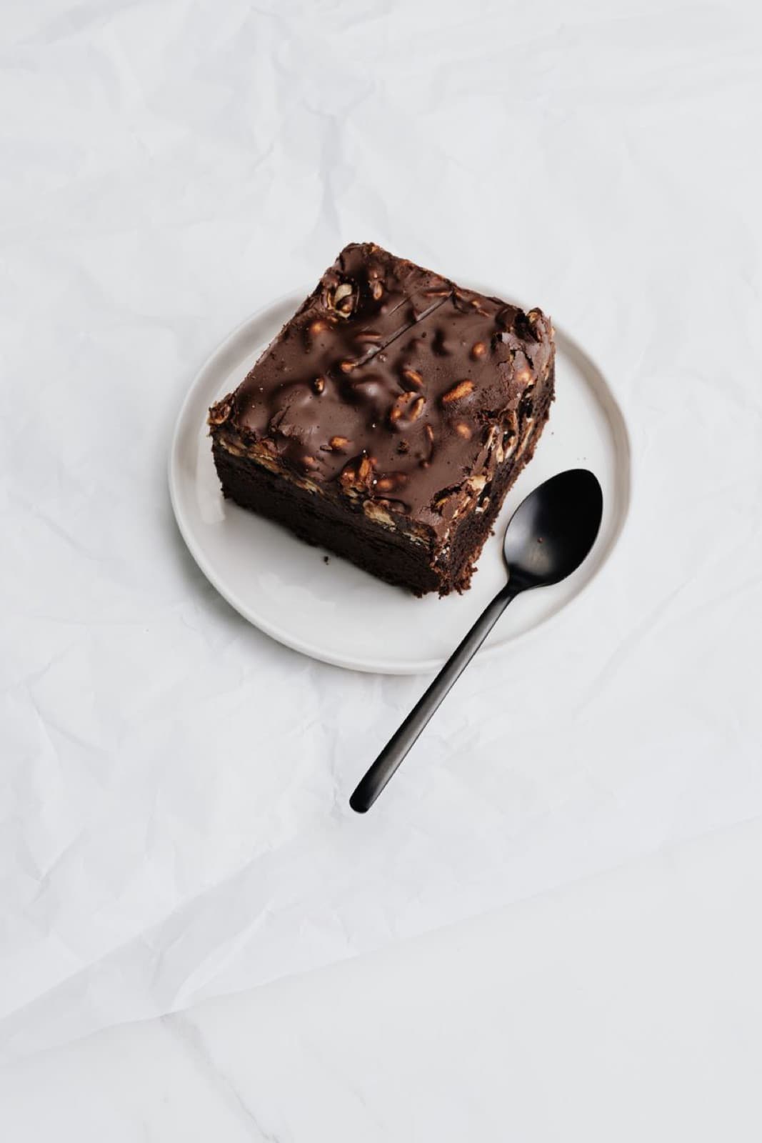 Beyaz tabakta tek brownie karesi ve siyah kaşık