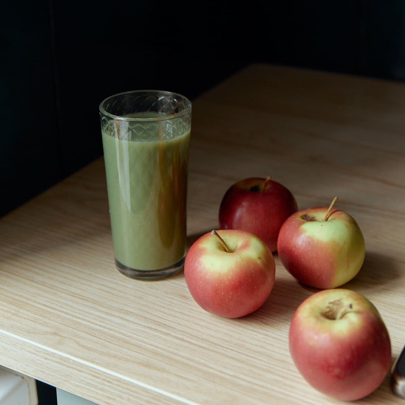 Açık ahşap masada düz cam bardakta yeşil elmalı smoothie, yanında kırmızı elmalar