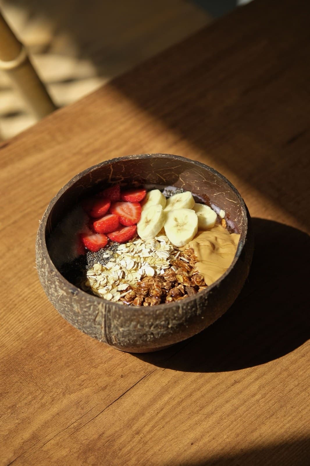 Hindistan cevizi kâsede smoothie, üzerinde muz dilimleri, çilek ve fıstık ezmesi