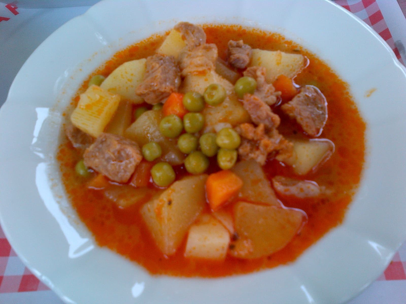 Beyaz tabakta kuşbaşı et, patates, havuç ve bezelyeyle salçalı sulu yemek